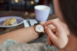 Frau fässt die Krone ihrer Hentschel Uhr an mit Cafebecher und Kuchen im Hintergrund – Produktfotograf Hamburg