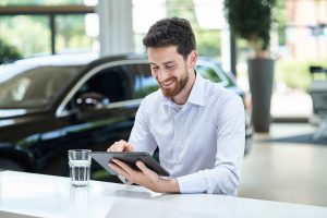 Mann laechelt am Tablet in einem Autohaus – People Fotograf Hamburg